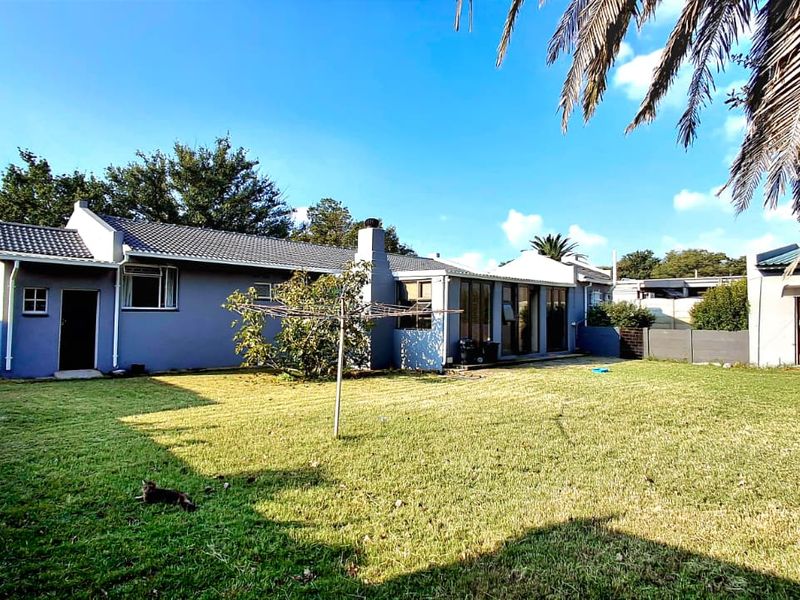 Rear view of the house featuring a spacious lawn, tiled roof, chimney, and sliding glass doors leading to the backyard.