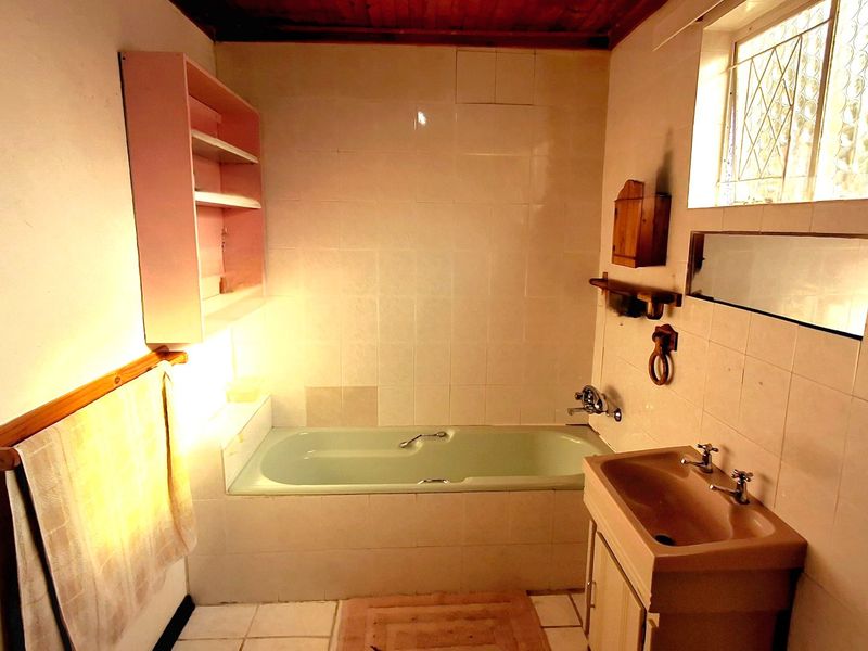 A dated bathroom featuring a built-in bathtub, vanity basin, tiled walls, and a timber ceiling with a glass block window.