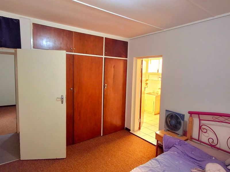 A bedroom featuring built-in wooden cupboards, carpeted flooring, and direct access to an adjoining bathroom.