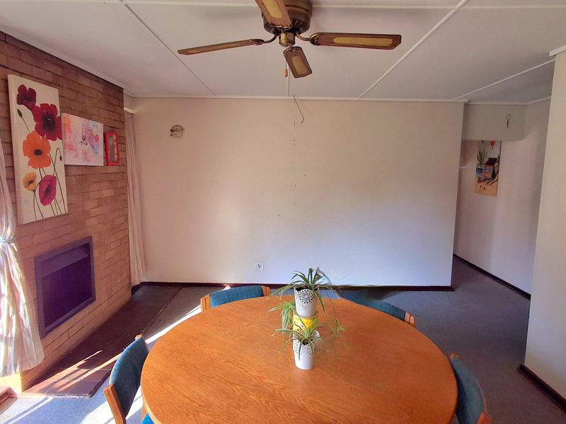 A living area featuring a brick fireplace, ceiling fan, and large window, offering a dated interior space with potential for modernization.