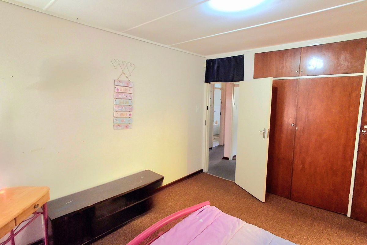 A bedroom featuring built-in wooden cupboards and carpeted flooring, providing a functional space with direct access to the hallway.