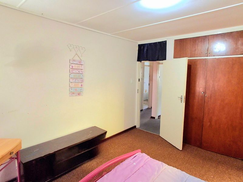 A bedroom featuring built-in wooden cupboards and carpeted flooring, providing a functional space with direct access to the hallway.