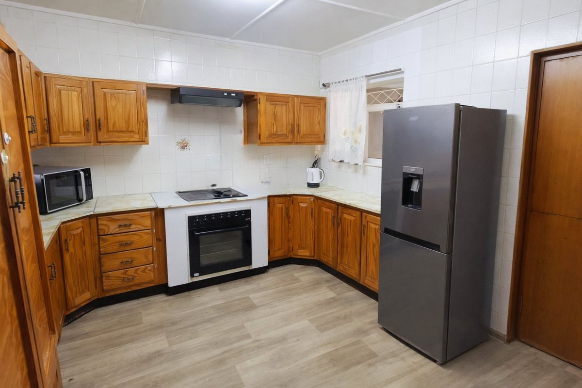 A functional kitchen featuring wooden cabinetry, laminate countertops, built-in oven with hob, and tiled splashbacks, offering a classic layout with modern flooring.