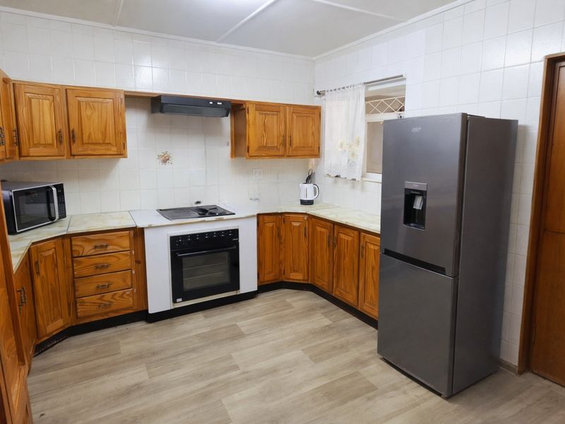 A functional kitchen featuring wooden cabinetry, laminate countertops, built-in oven with hob, and tiled splashbacks, offering a classic layout with modern flooring.