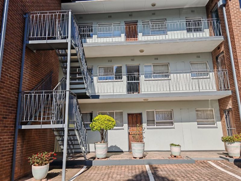 Rear view of a multi-story apartment building featuring external metal staircases, balcony access, and a paved ground-level parking area.