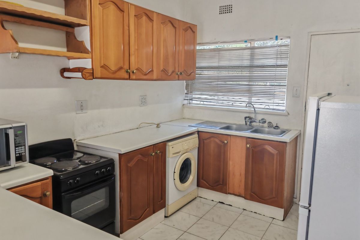 A functional kitchen featuring wooden cabinetry, laminate countertops, a stainless steel sink, and built-in appliances, offering potential for modernization and cosmetic updates.