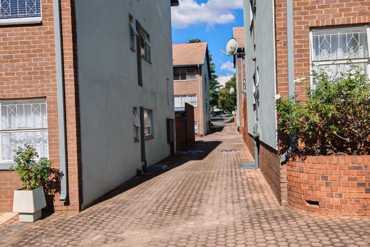 A view of the paved driveway and access path between two apartment building blocks, featuring brick and plastered exterior finishes.