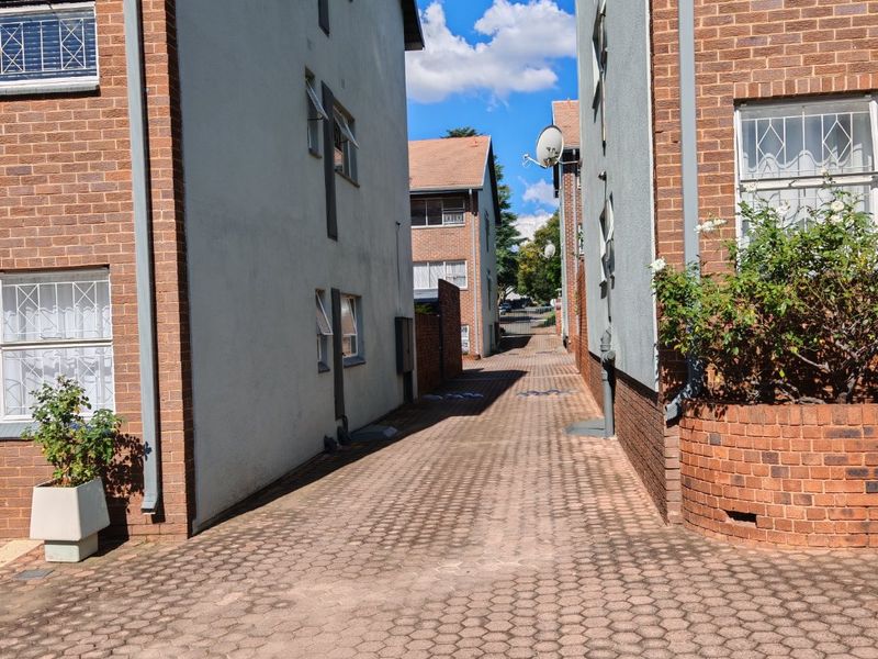 A view of the paved driveway and access path between two apartment building blocks, featuring brick and plastered exterior finishes.