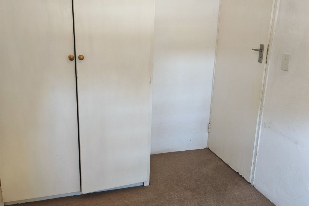 An empty bedroom featuring built-in cupboards, carpeted flooring, and a wall-mounted electrical distribution board.
