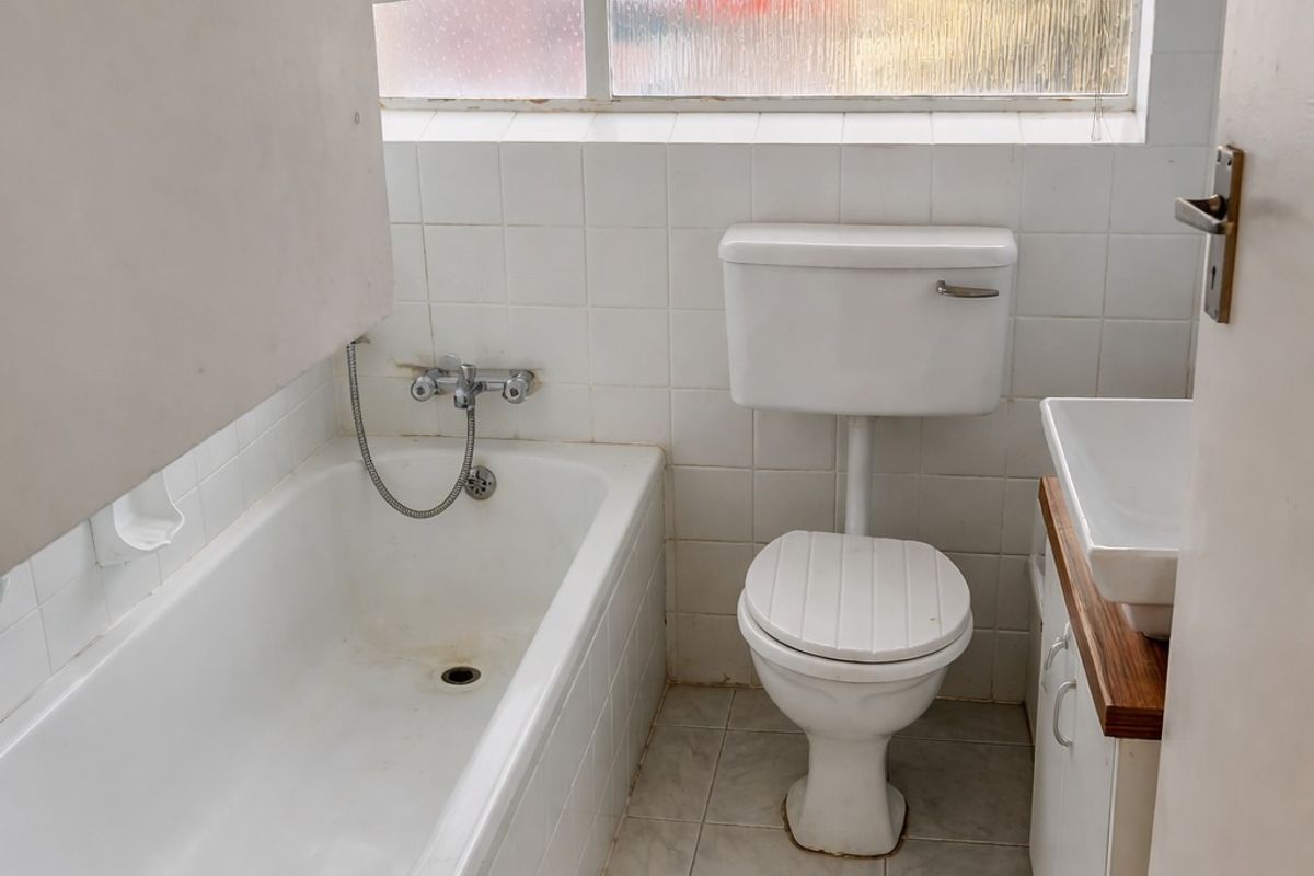 A compact bathroom featuring a standard bathtub, toilet, and vanity basin with tiled finishes, requiring cosmetic updates to modernize the space.