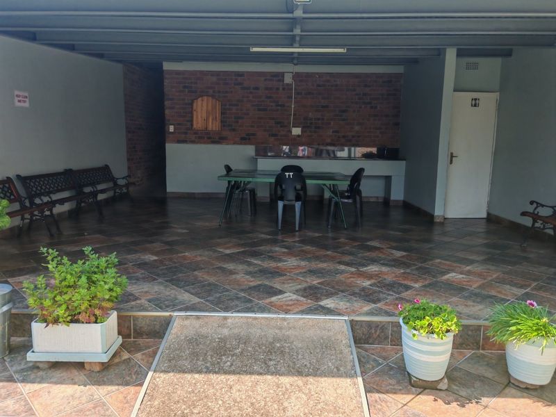 A covered outdoor patio area featuring tiled flooring, a brick accent wall, and a built-in counter, suitable for outdoor dining and entertainment.