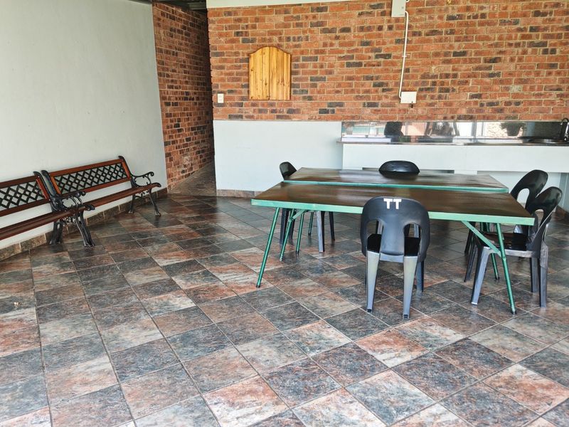 A covered outdoor patio area featuring exposed brick walls, durable tiled flooring, and a built-in sink with countertop space, ideal for outdoor entertaining.