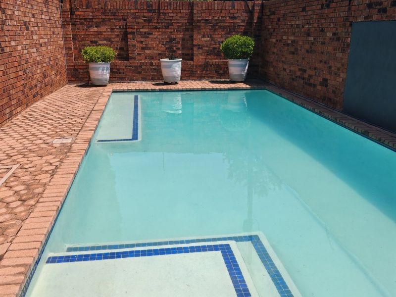 A private swimming pool area featuring a paved surround and high brick boundary walls with integrated electric fencing for added security.