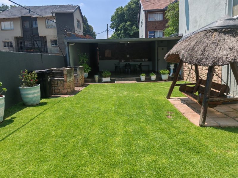 A well-maintained rear garden featuring a manicured lawn, a built-in braai area, and a covered patio space, ideal for outdoor entertaining.