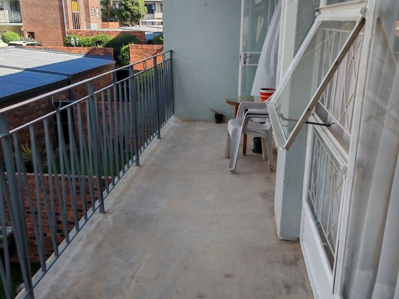 A covered balcony featuring a metal balustrade and concrete flooring, offering an outdoor space with views of the surrounding apartment complex.