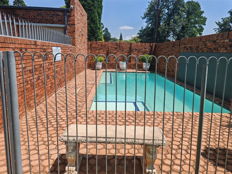 A private swimming pool area enclosed by brick walls and metal security fencing, featuring a paved surround.
