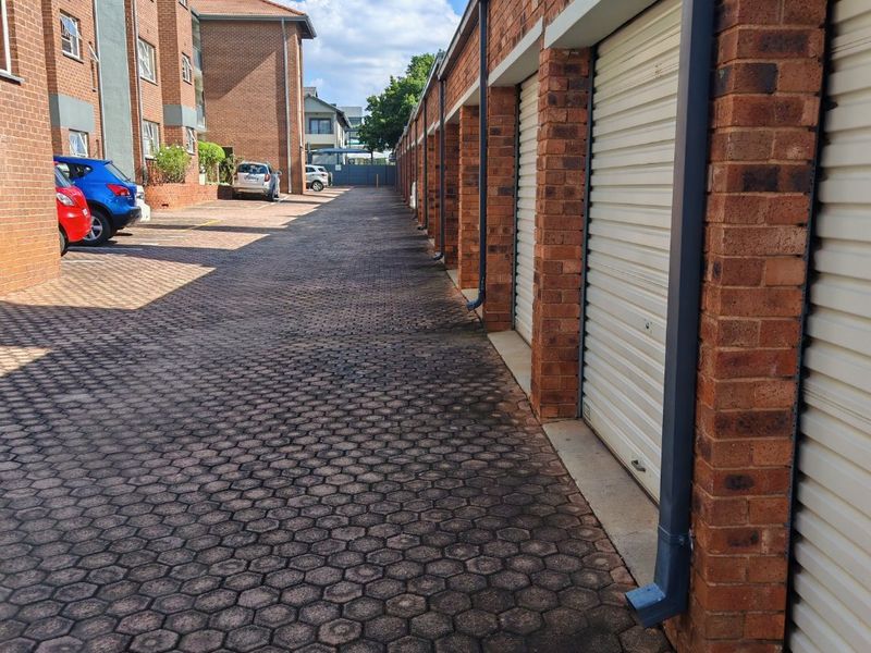 Exterior view of a row of brick garages with roller shutter doors and a paved driveway in an apartment complex.