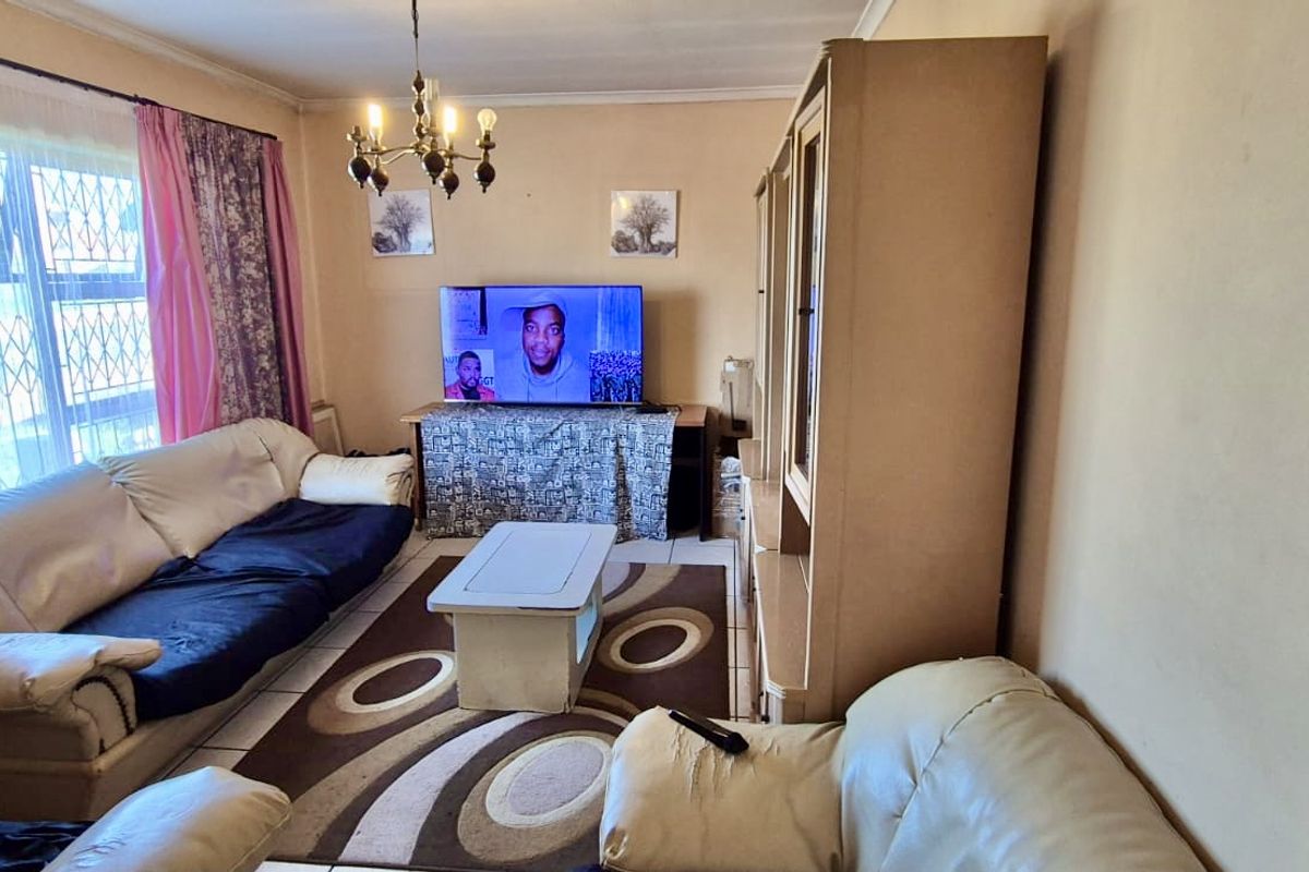 A living room featuring tiled flooring, a central chandelier, and security bars on the window.