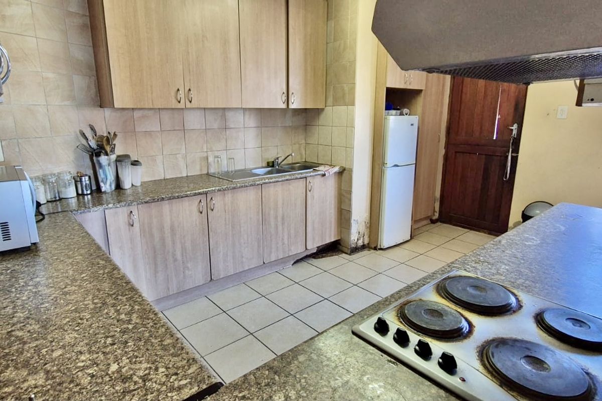 A functional kitchen featuring laminate cabinetry, granite-look countertops, a built-in electric hob, and tiled flooring with direct access to an exterior door.