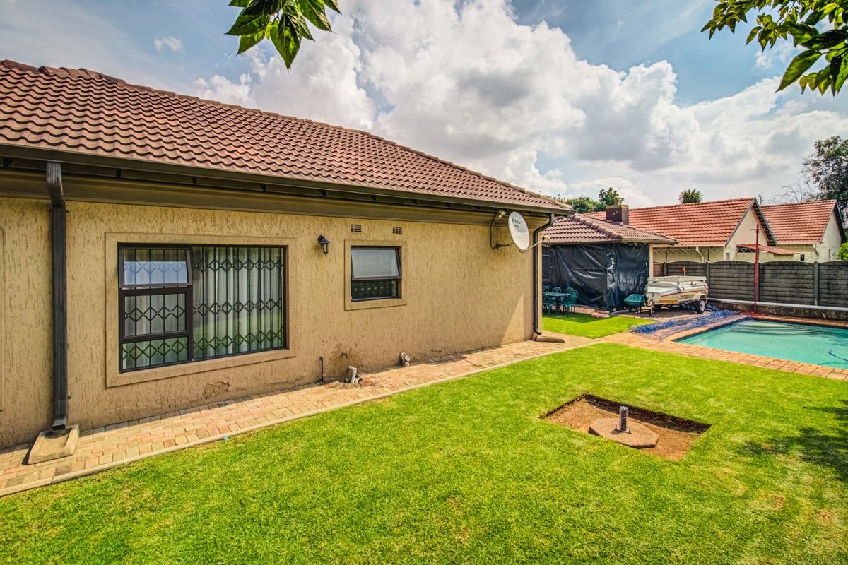 Rear view of the property featuring a textured plaster facade, security-fitted windows, a paved walkway, and a swimming pool set within a lawned garden.