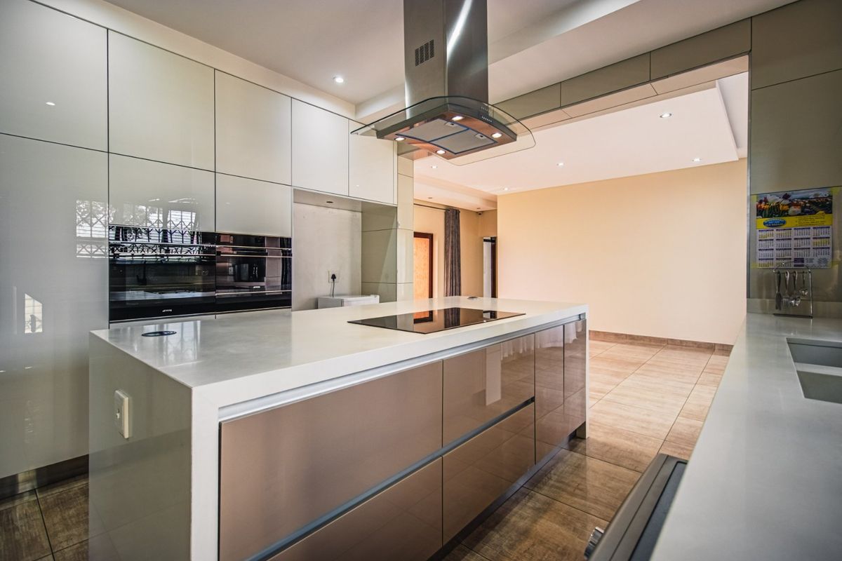 Modern kitchen featuring a central island with an induction hob, integrated extractor fan, high-gloss cabinetry, and sleek built-in appliances.