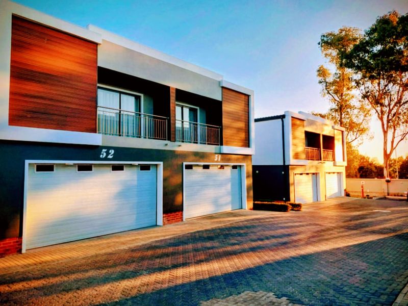 Modern residential townhouse complex featuring double garages, timber-clad facades, and upper-level balconies with a paved driveway approach.