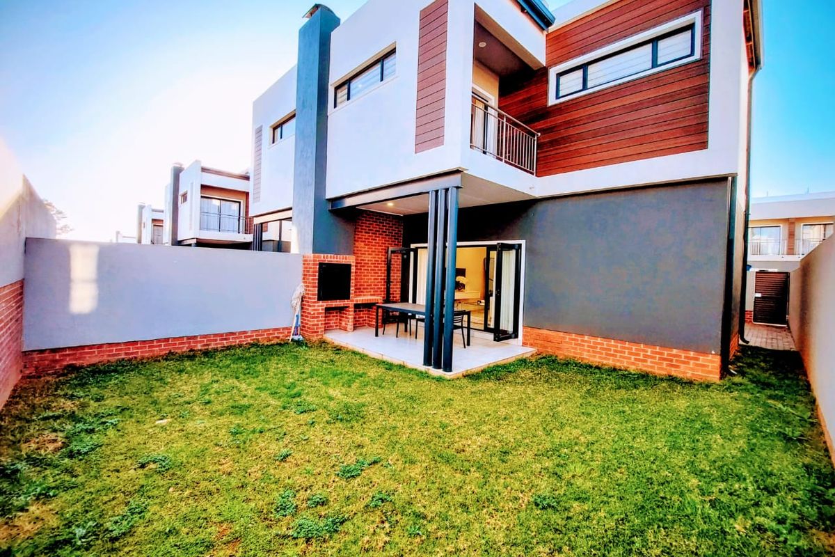 Modern double-storey rear elevation featuring a covered patio with built-in braai, balcony, and a private garden area.