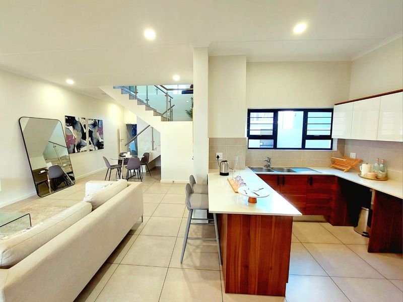 Modern open-plan living area featuring a contemporary kitchen with island, tiled floors, and a sleek staircase with glass balustrade.