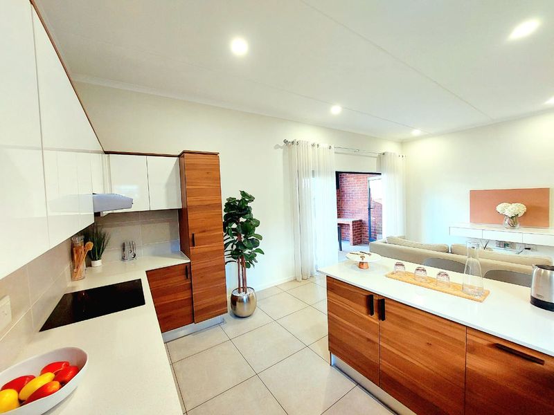 Modern open-plan kitchen and living area featuring sleek wood and white cabinetry, stone countertops, integrated hob, and direct access to an outdoor patio.