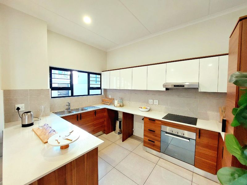 Modern kitchen featuring sleek white and wood-tone cabinetry, stone countertops, integrated stainless steel appliances, and a tiled splashback.
