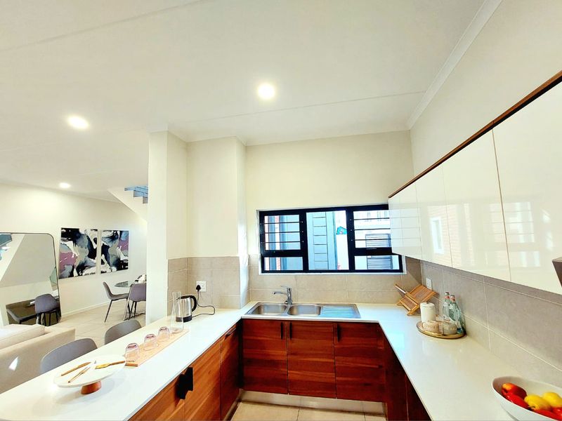 Modern kitchen featuring sleek white upper cabinetry, warm wood-toned lower cabinets, stone countertops, and a double sink with a tiled splashback.