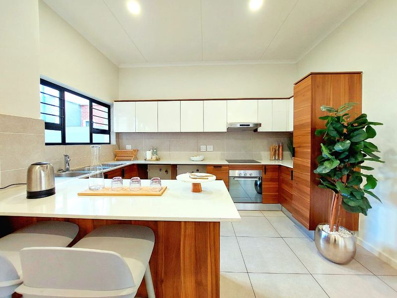Modern kitchen featuring sleek wood and white cabinetry, stone countertops, integrated appliances, and tiled flooring with a functional breakfast bar layout.