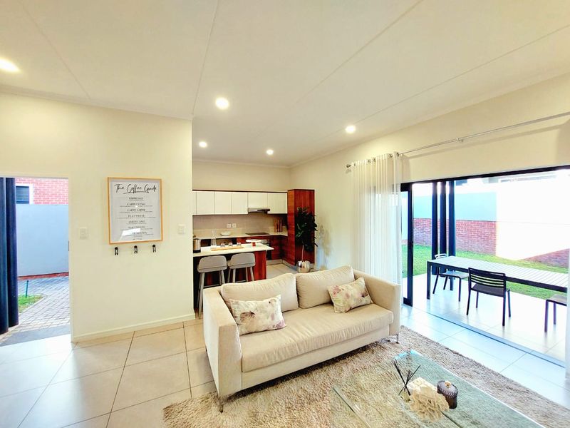 Bright open-plan living area featuring a modern kitchen with island, recessed lighting, and large sliding doors leading to an outdoor patio space.