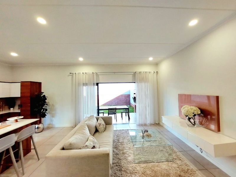 Spacious open-plan living area featuring tiled floors, recessed lighting, and seamless flow to an outdoor patio through large sliding glass doors.