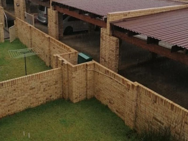 Rear view of the townhouse property featuring a private lawn area enclosed by brick boundary walls and a covered carport structure.