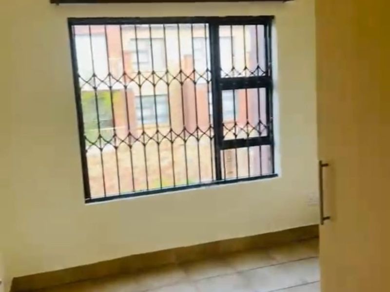 An empty bedroom featuring tiled flooring, a built-in cupboard, and a window fitted with a security gate.