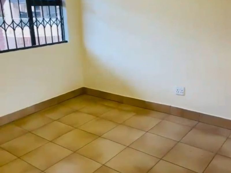 An empty bedroom featuring tiled flooring and a window fitted with security bars.