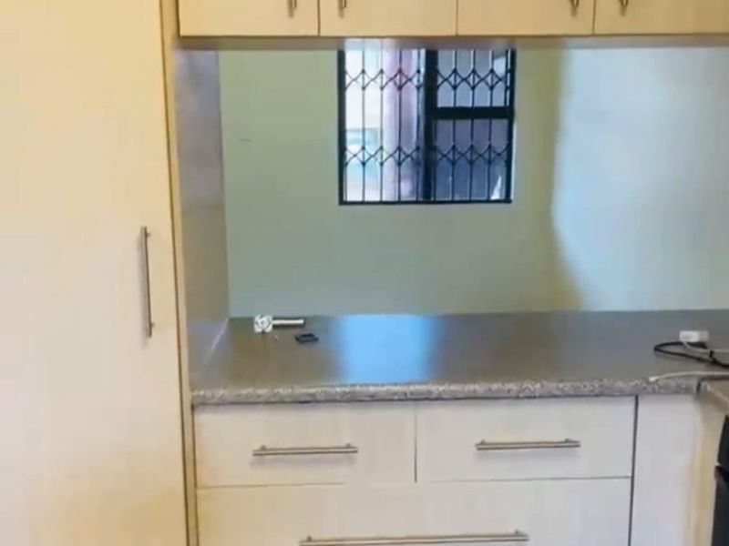 A compact kitchen area featuring built-in cabinetry, laminate countertops, and a window with a security gate.