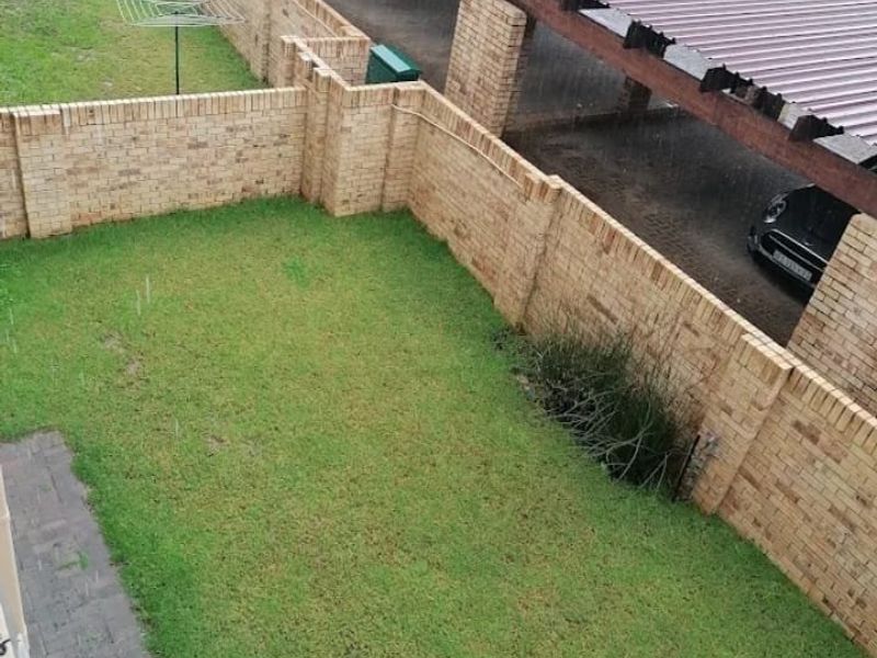 An elevated view of a private rear garden featuring a lawn, brick boundary walls, and an adjacent carport area.