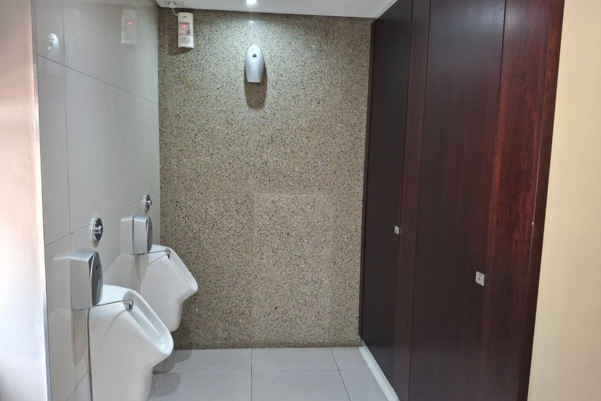 A clean, modern commercial restroom featuring wall-mounted urinals, tiled surfaces, a stone-textured feature wall, and private partitioned cubicles.