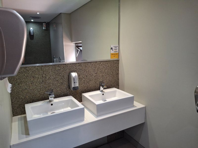 Modern commercial bathroom featuring a double vanity with vessel sinks, chrome faucets, and a large wall-mounted mirror.