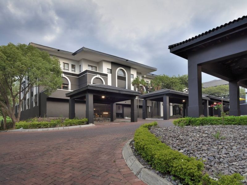 Professional exterior view of a commercial property featuring a covered porte-cochere, paved driveway, and well-maintained landscaped garden beds.