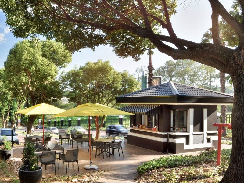 A well-maintained outdoor kiosk area featuring a paved patio, service window, and shaded seating space under mature trees.