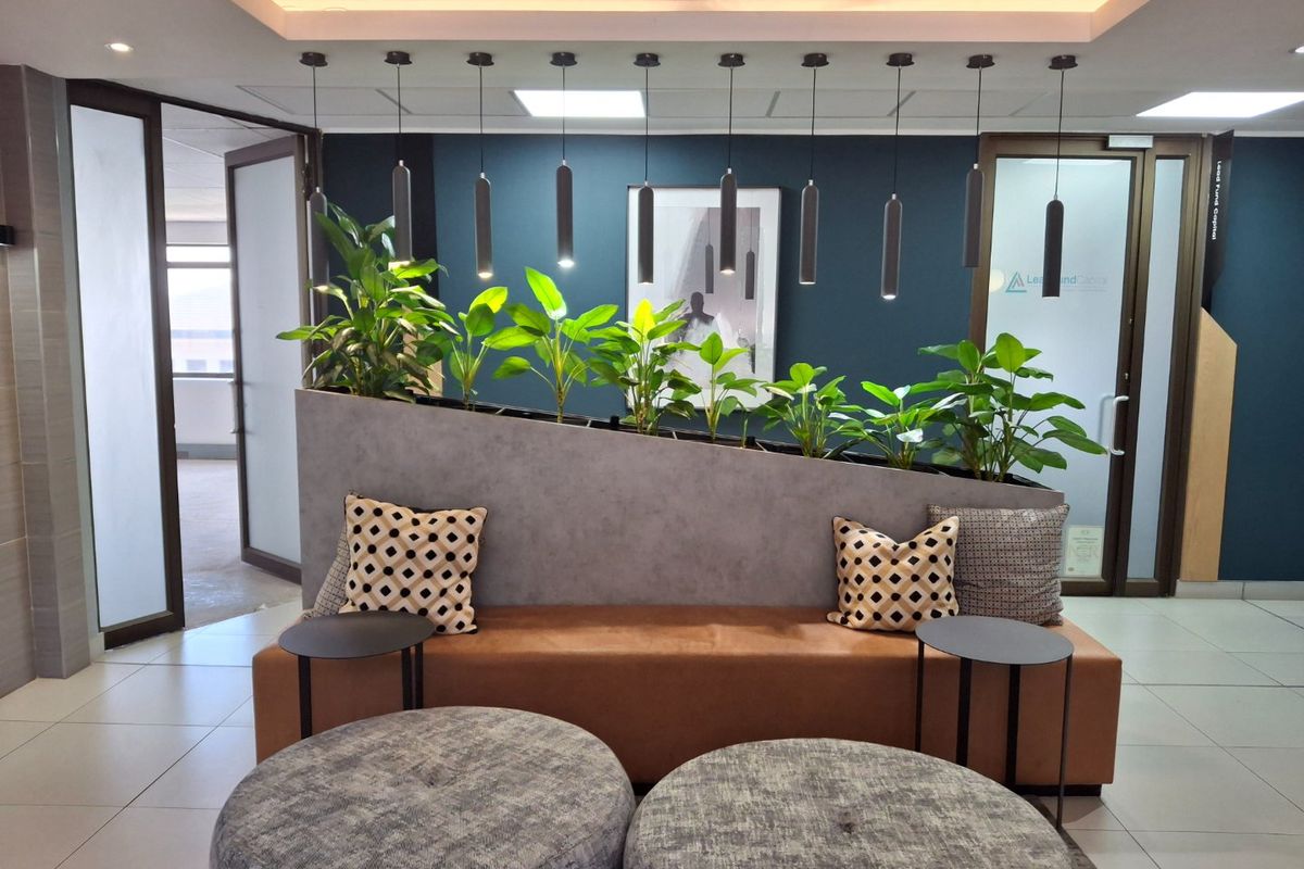 Modern commercial reception area featuring tiled flooring, recessed ceiling lighting, stylish pendant lights, and a built-in planter partition with glass entry doors.