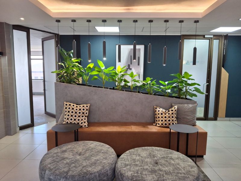 Modern commercial reception area featuring tiled flooring, recessed ceiling lighting, stylish pendant lights, and a built-in planter partition with glass entry doors.