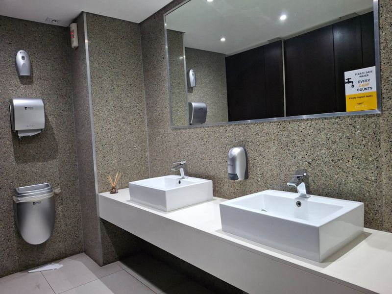 Modern commercial bathroom featuring a double vanity with vessel sinks, stone wall cladding, and high-quality chrome fixtures.