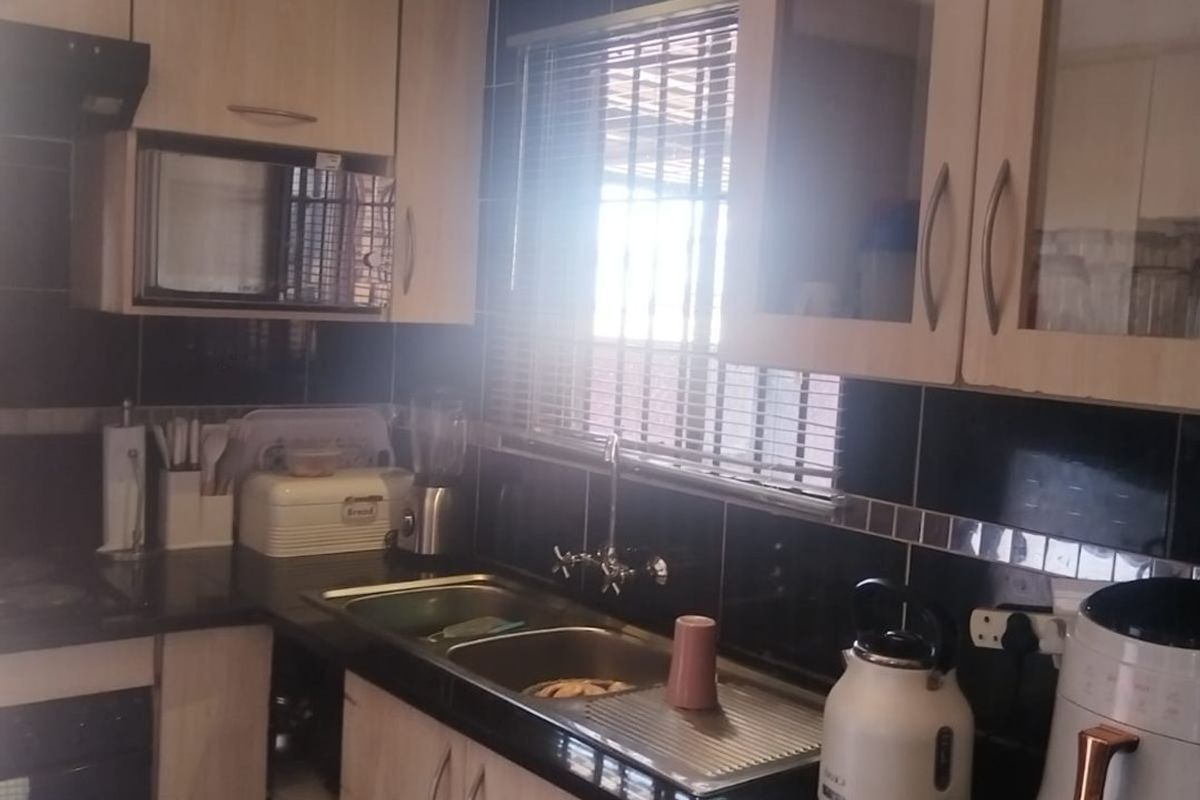 A functional kitchen featuring light wood cabinetry, black granite countertops, a double sink, and a tiled backsplash with built-in microwave and extractor fan.
