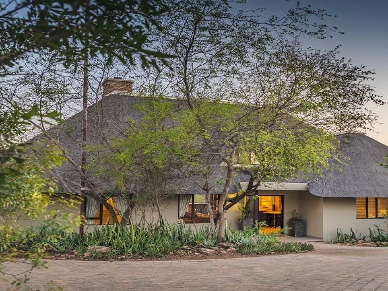 A charming farm-style residence featuring a traditional thatched roof, a brick-paved driveway, and established garden landscaping at the front entrance.