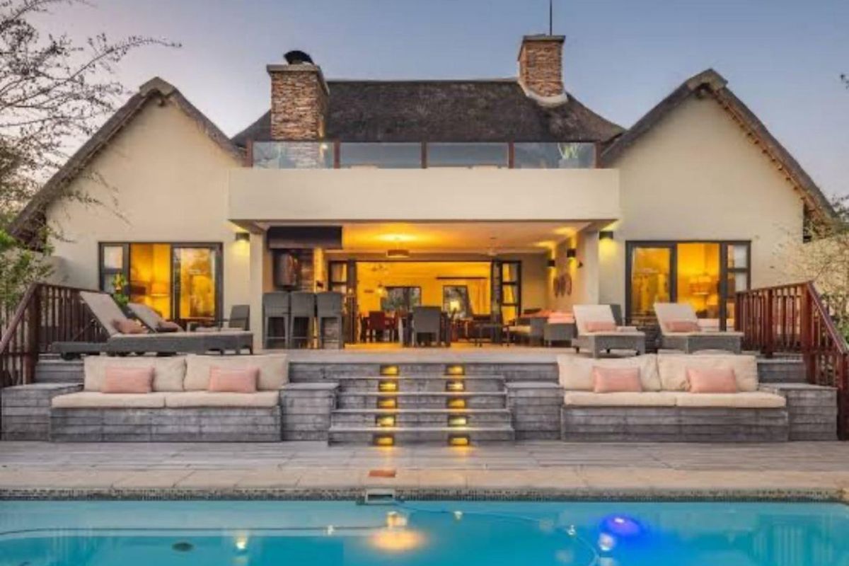 Rear view of a luxury farm property featuring a swimming pool, expansive timber deck with built-in seating, and a thatched roof residence.