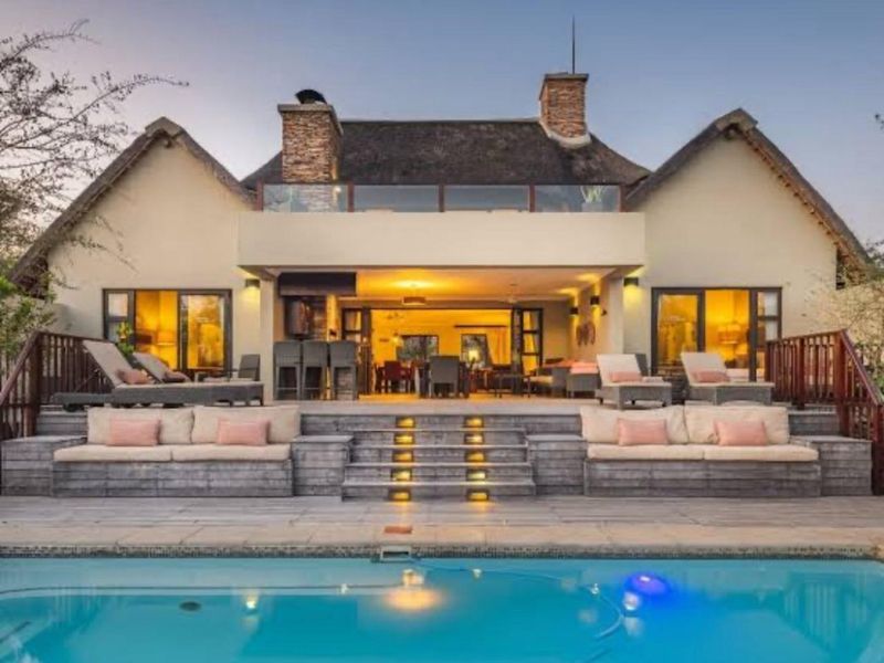 Rear view of a luxury farm property featuring a swimming pool, expansive timber deck with built-in seating, and a thatched roof residence.